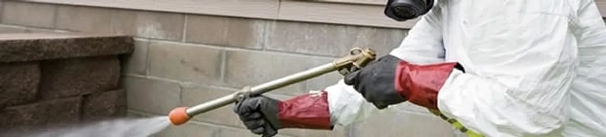 Pest control technician applying exterior insect treatment along a home foundation in Nashville, TN