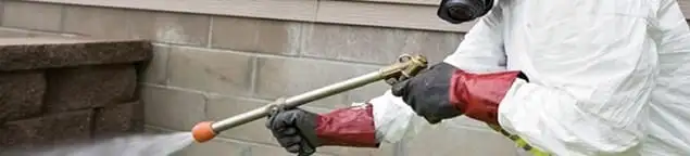 Pest control technician applying exterior insect treatment along a home foundation in Nashville, TN