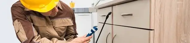 Roach exterminator applying treatment under kitchen cabinets in Nashville, TN