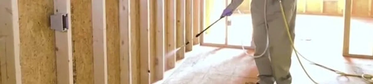 Termite treatment technician applying spray along framing and unfinished walls in Nashville, TN