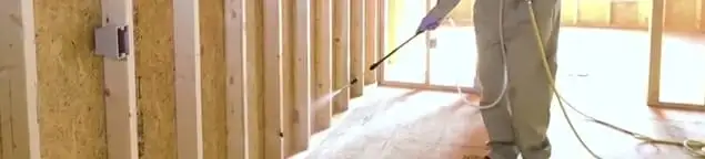 Termite treatment technician applying spray along framing and unfinished walls in Nashville, TN